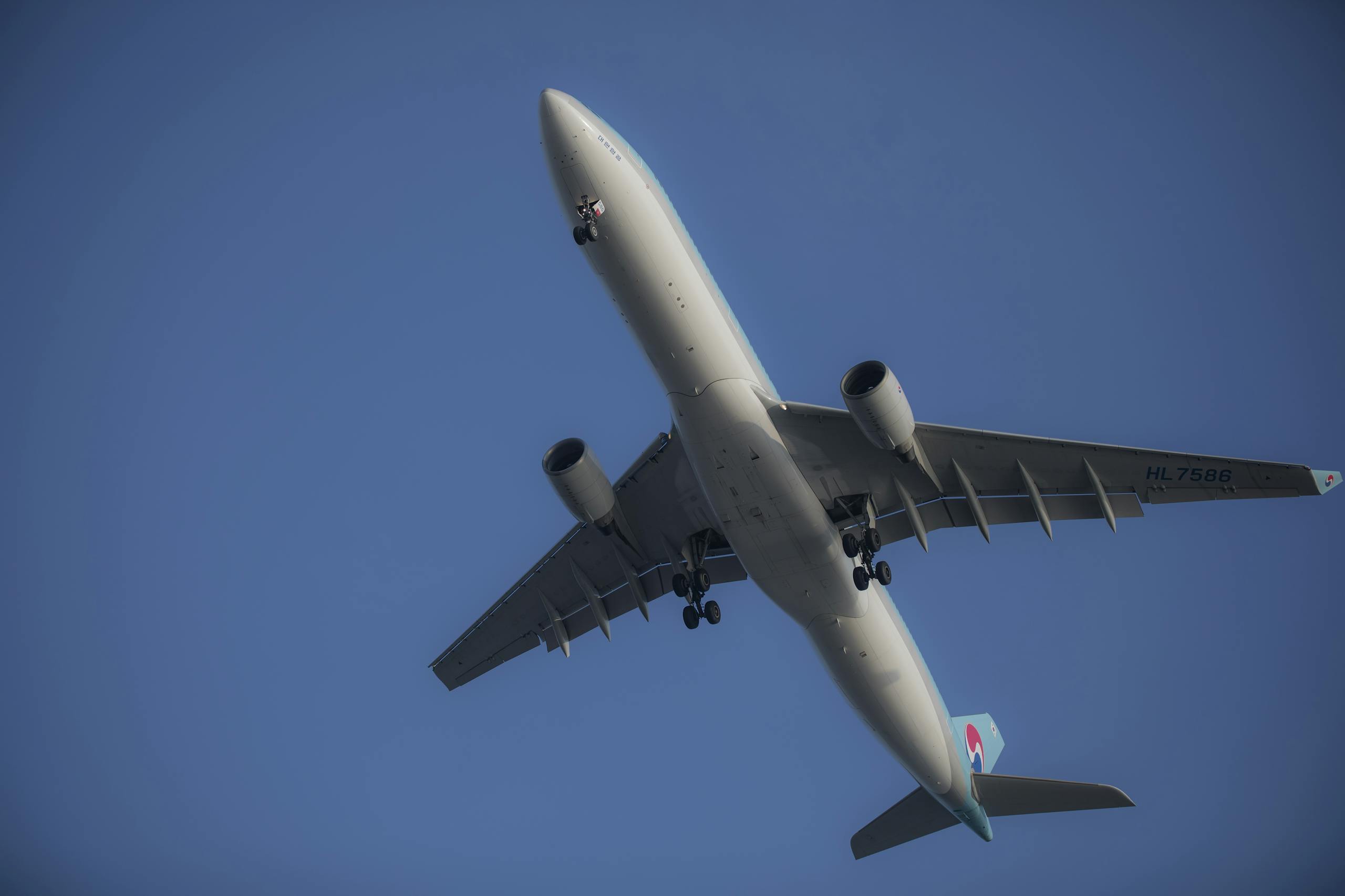 A commercial airplane flying overhead, captured from below against a clear blue sky.